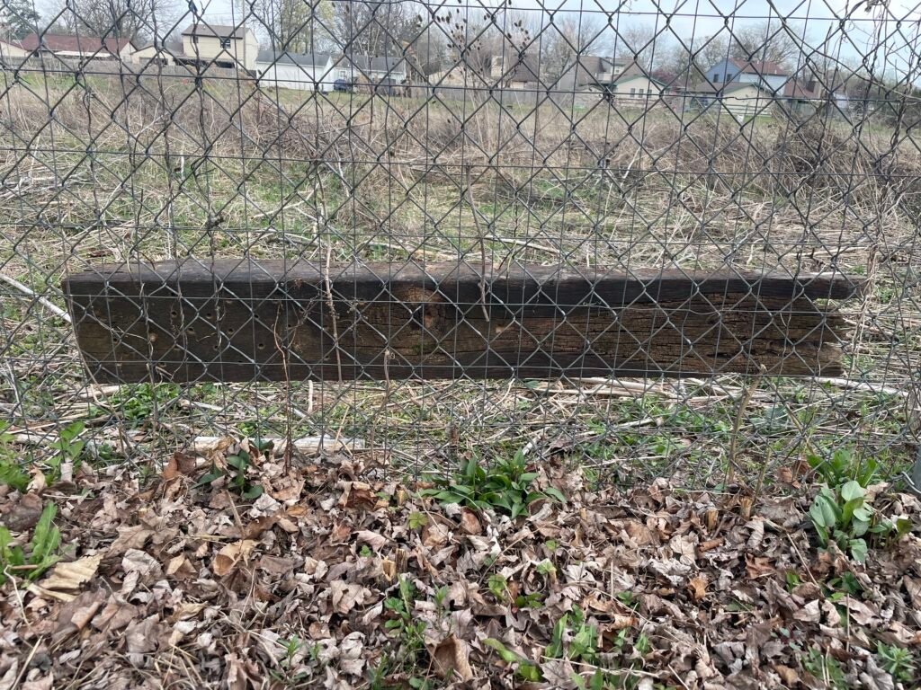 A large piece of wood with holes hung up on a fence, to create a mason bee hotel.