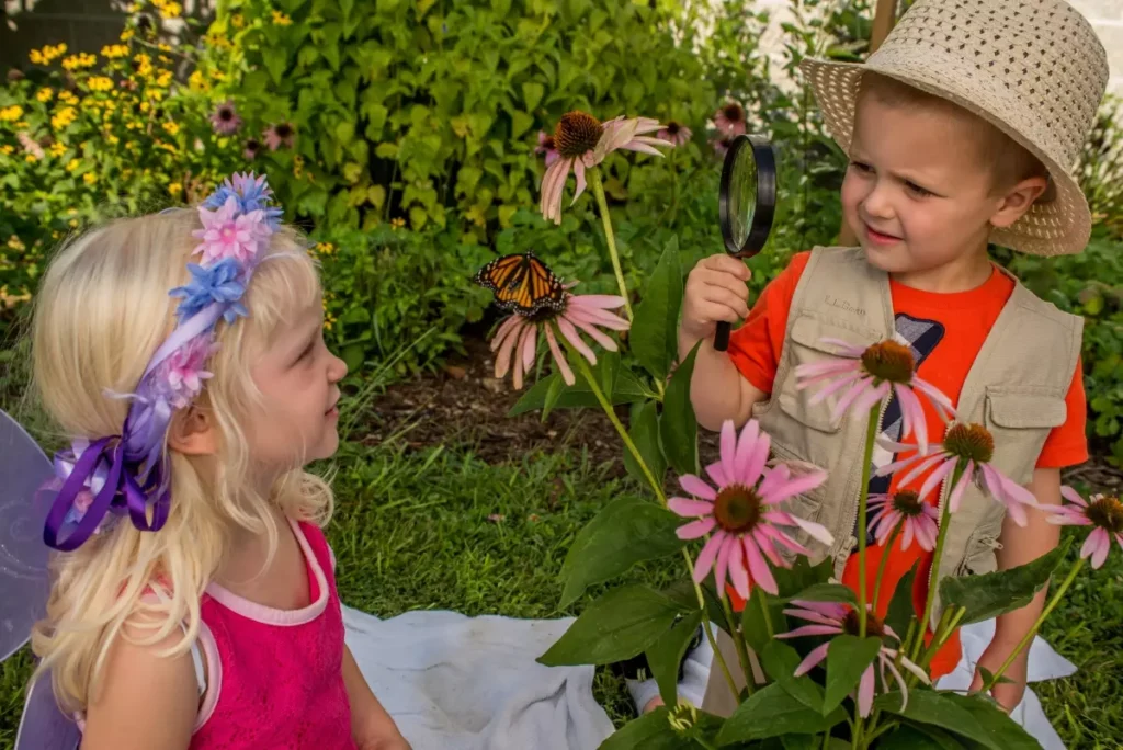 Two young children looking at a monarch butterfly on purple coneflower.
